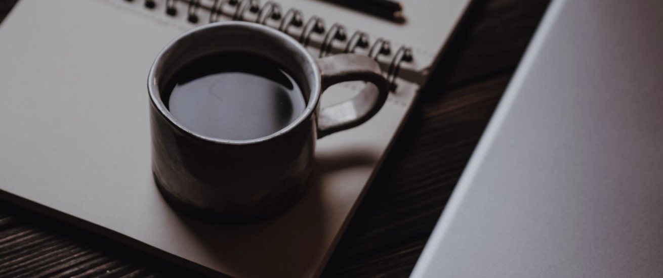Et arbejdsbord med notesbog, kaffe og en computer, hvor en ny guide bliver skrevet og læst igennem
